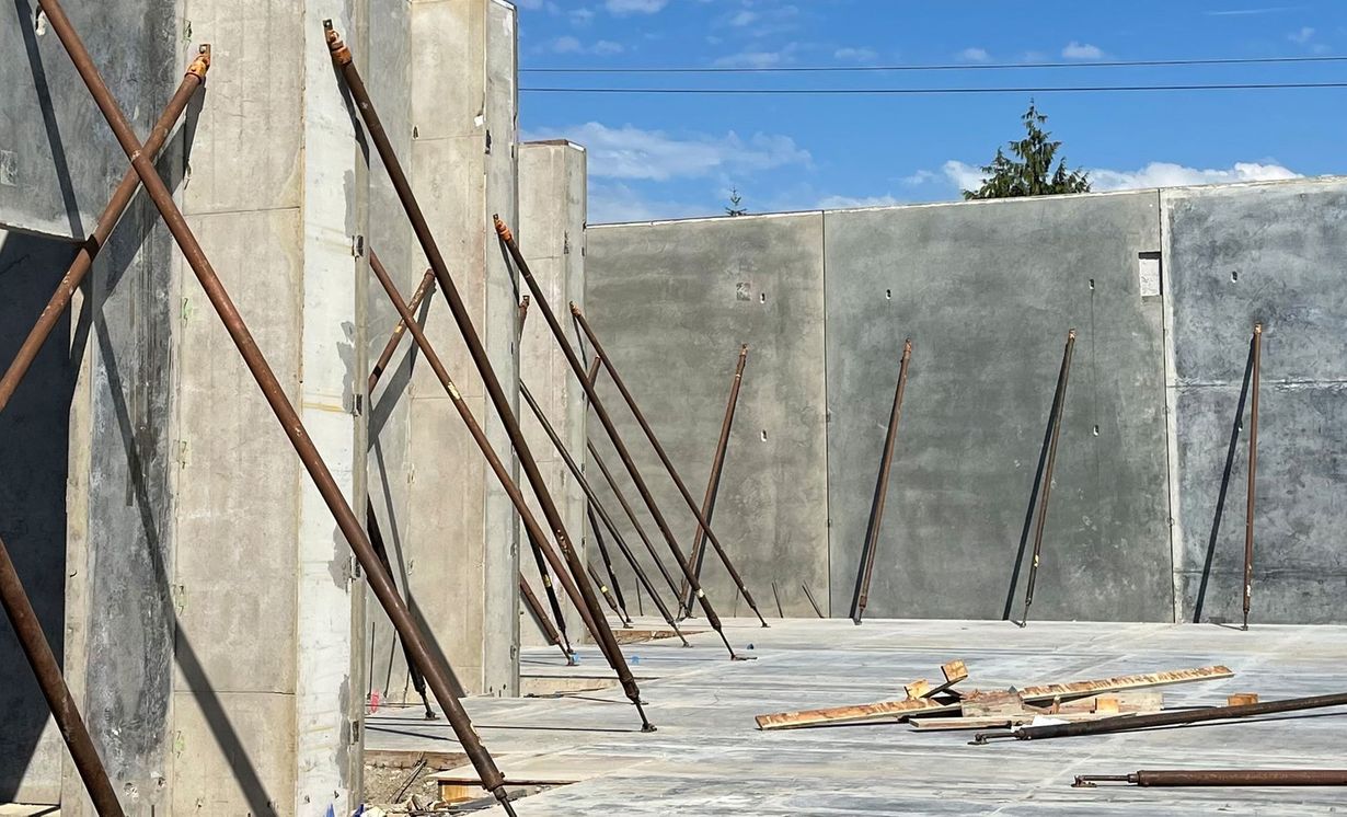Concrete foundation walls with diagonal metal braces at a construction site under a blue sky.