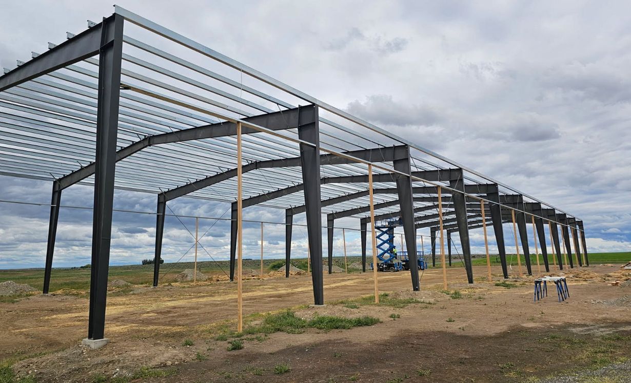 Steel frame building under construction on a cloudy, open field site