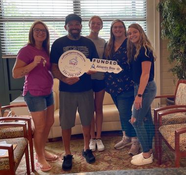 Five people stand indoors holding a large decorative key that says