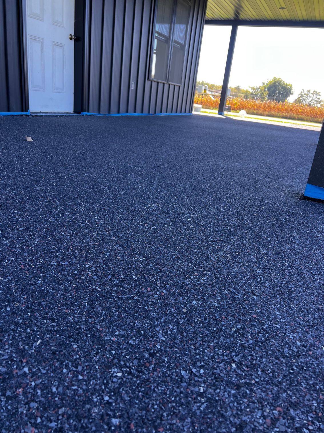 Dark blue pebble-like surface leading to a building with a white door and window. Sunny outdoor setting.