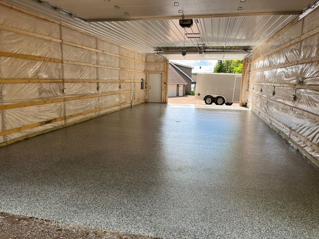 Empty garage with epoxy floor, insulated walls, and open door to an outdoor area with a trailer.