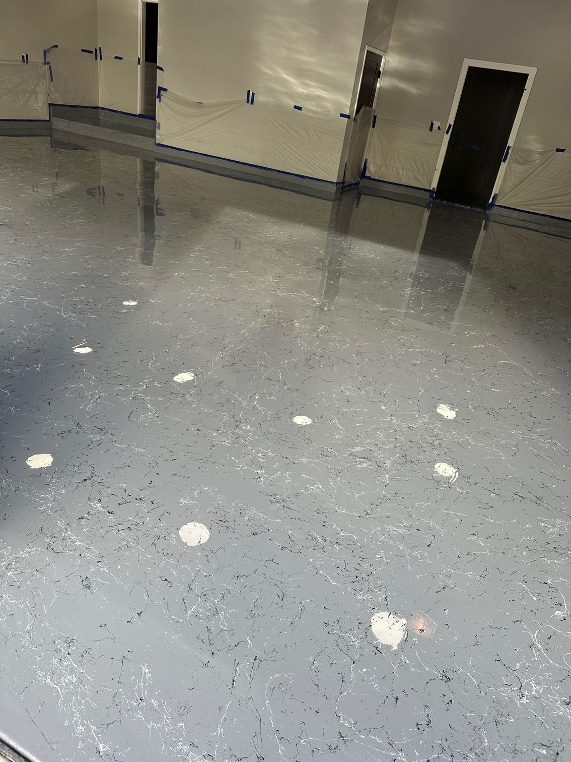 Gray speckled epoxy floor in a garage with recessed lights and a black door.
