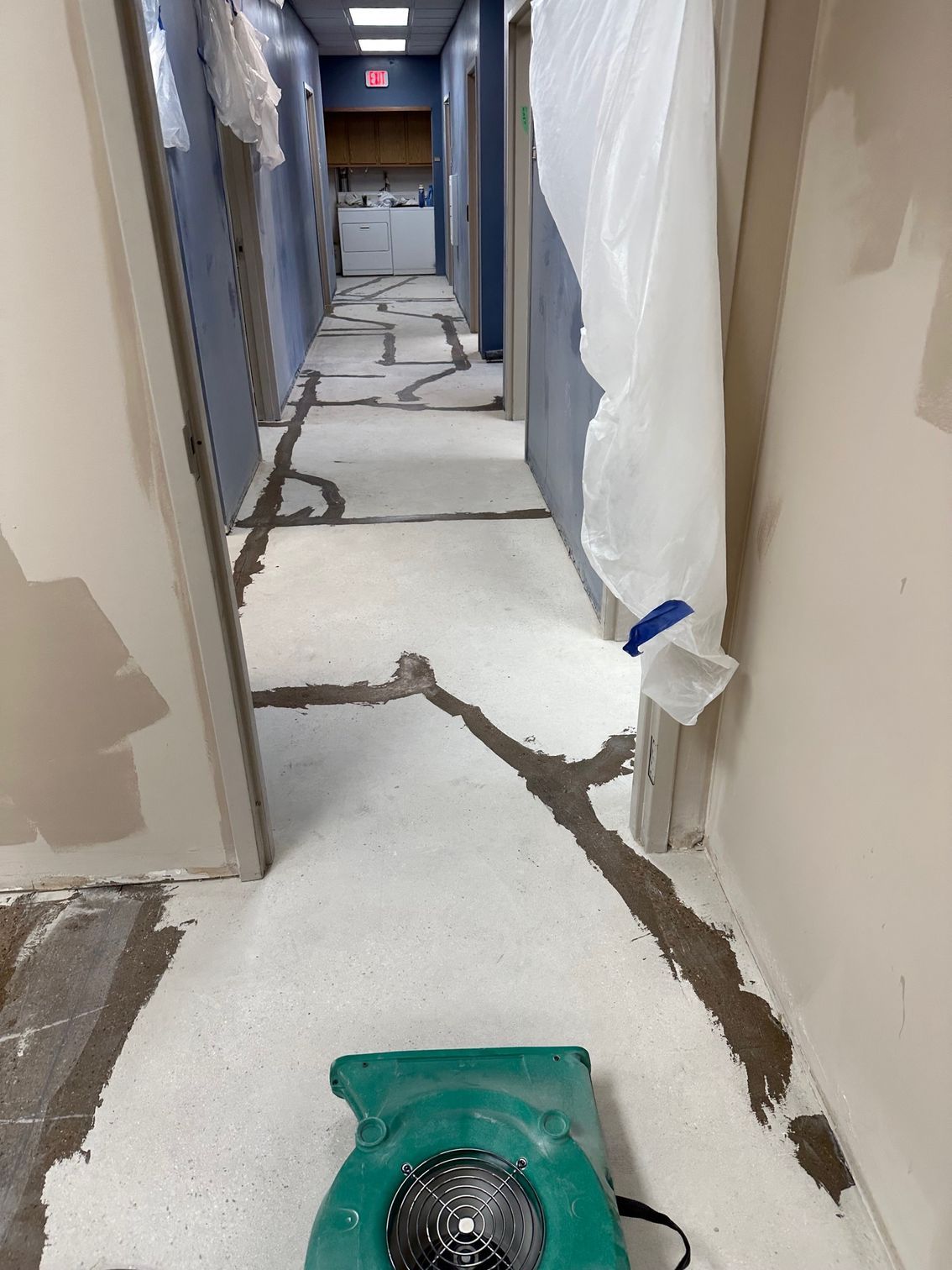 Hallway undergoing renovation with exposed flooring and a floor fan.