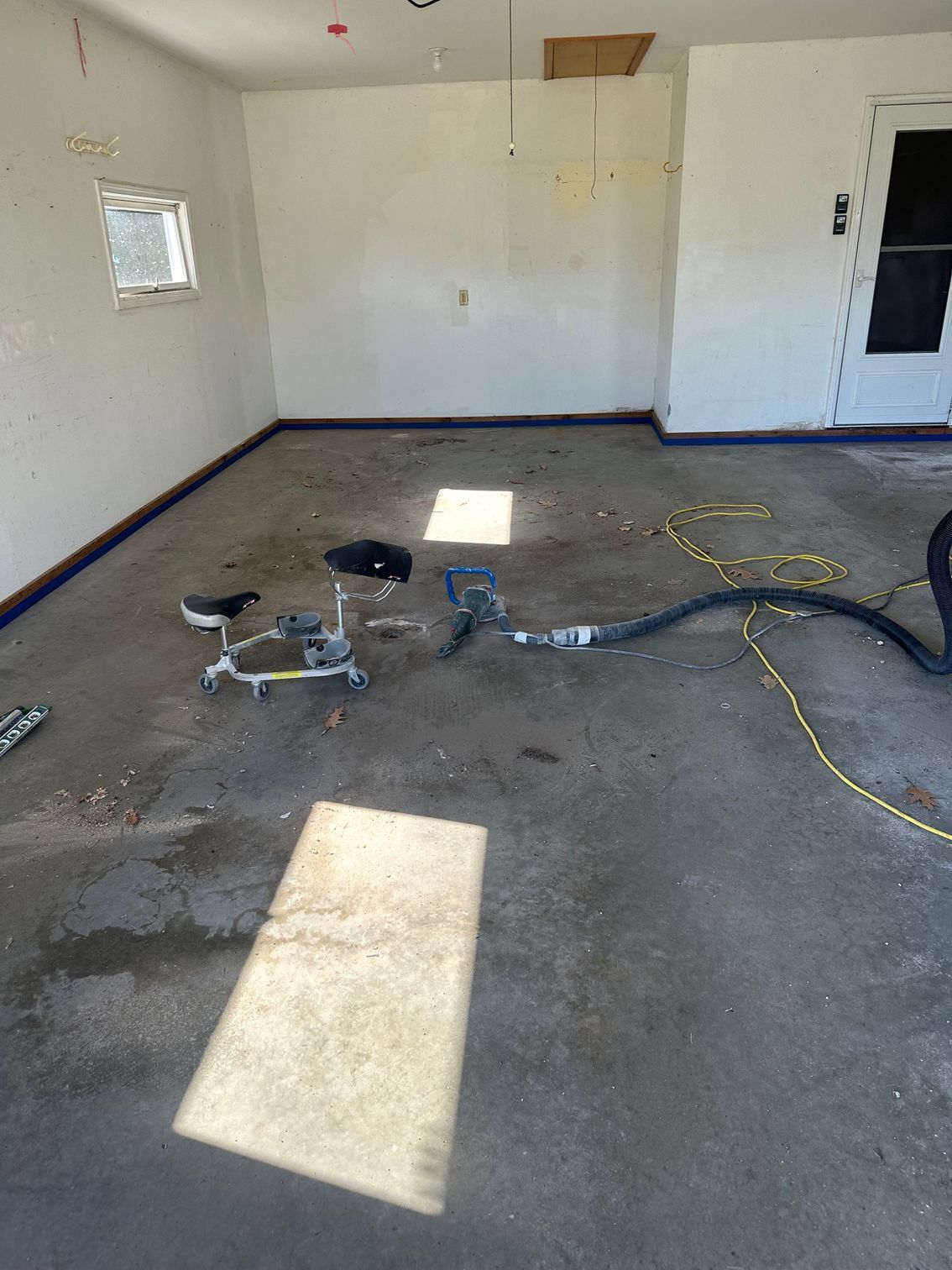Garage interior with equipment and concrete floor; white walls and a door are visible.