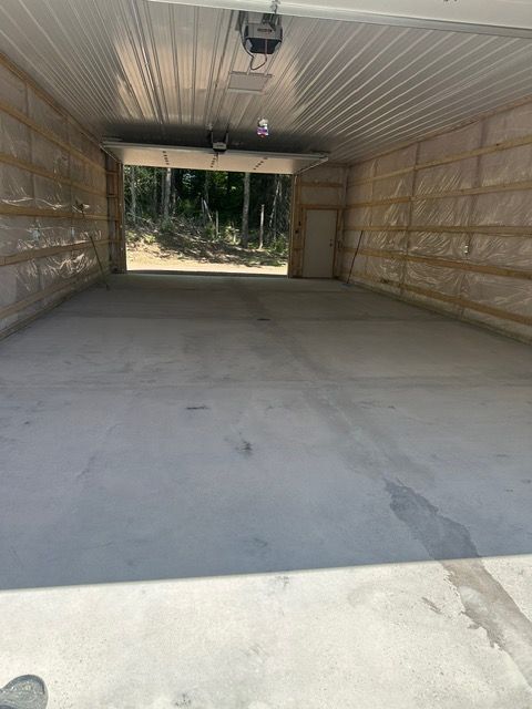 Empty garage interior with concrete floor, open door in the back, and exposed insulation on the walls.