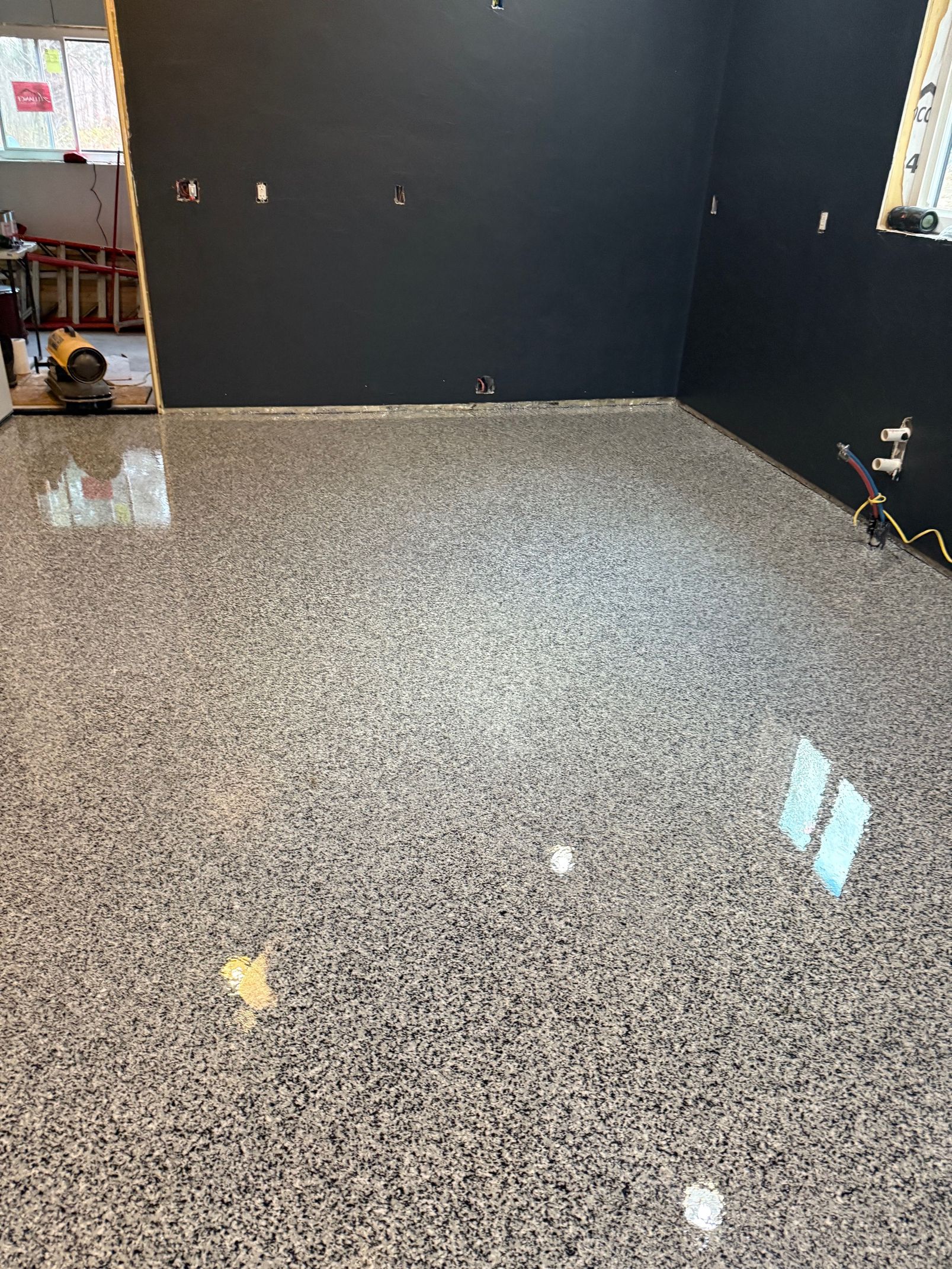 Epoxy-coated floor in a room with dark walls; flooring has a speckled gray and white pattern; some light reflections.