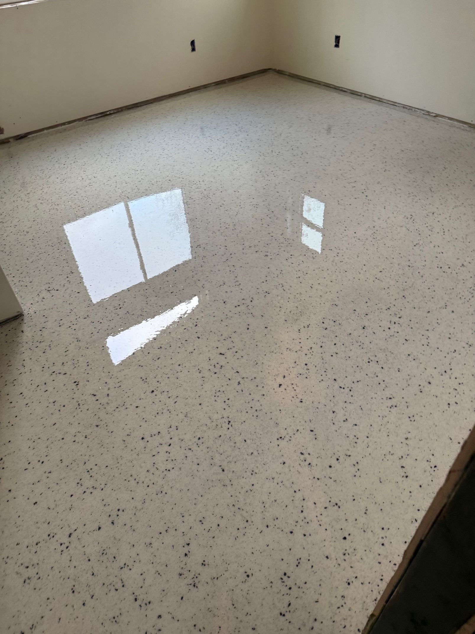 Room with a polished, speckled floor reflecting sunlight. White walls and a bare interior.