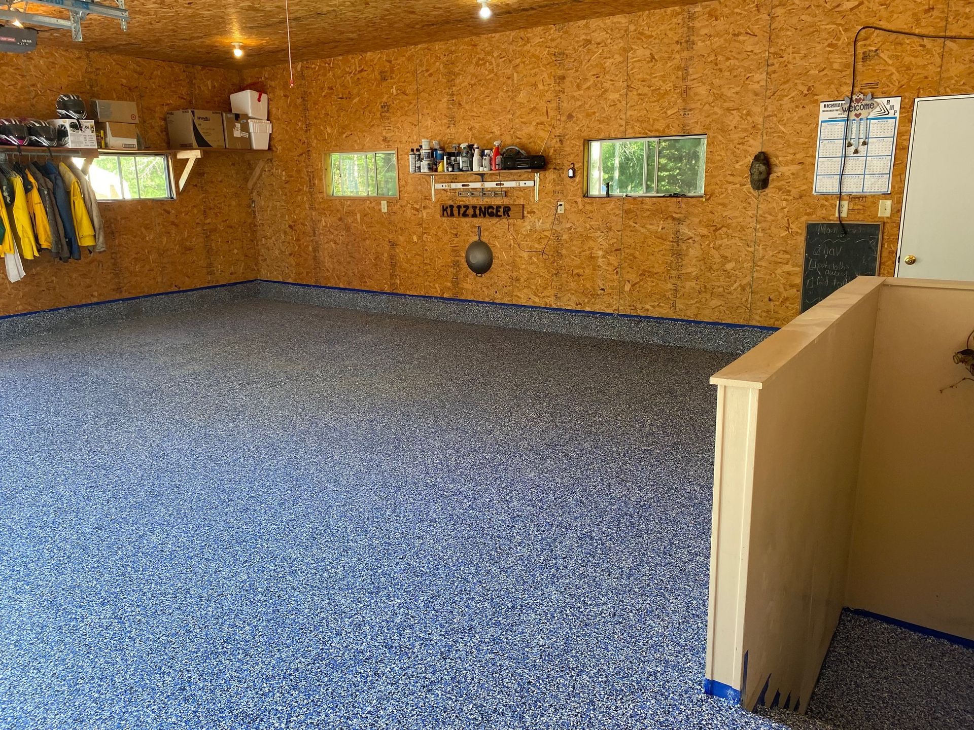 Garage with blue speckled epoxy floor, unfinished wood walls, and open windows.