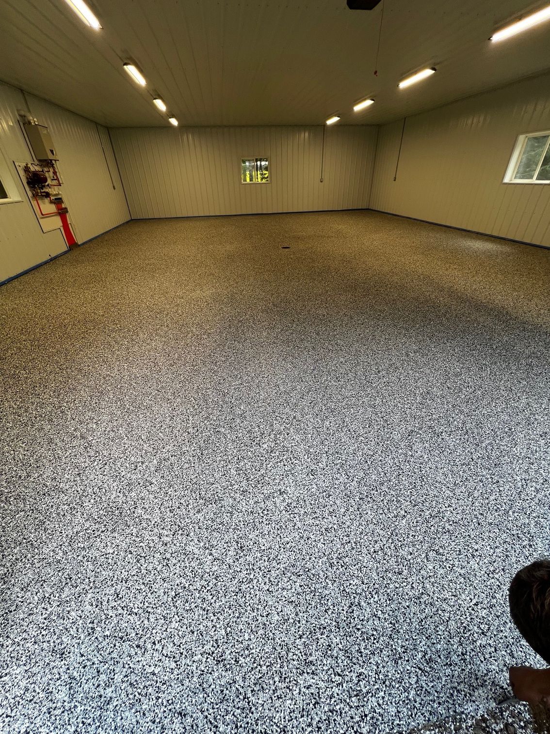 A spacious garage with a speckled gray floor, bright white walls, and overhead lighting.