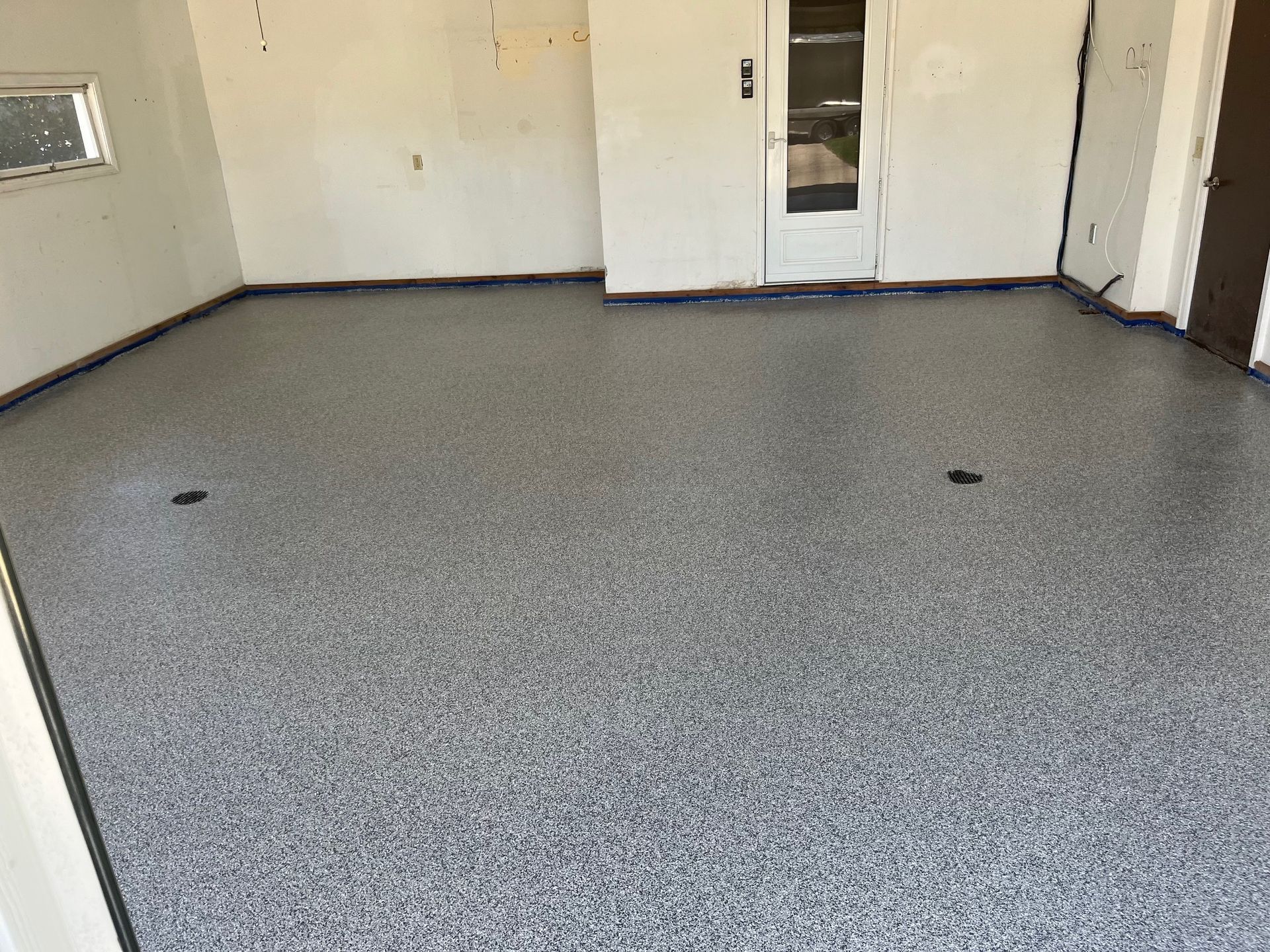 Garage with gray speckled epoxy flooring, white walls, and a door.