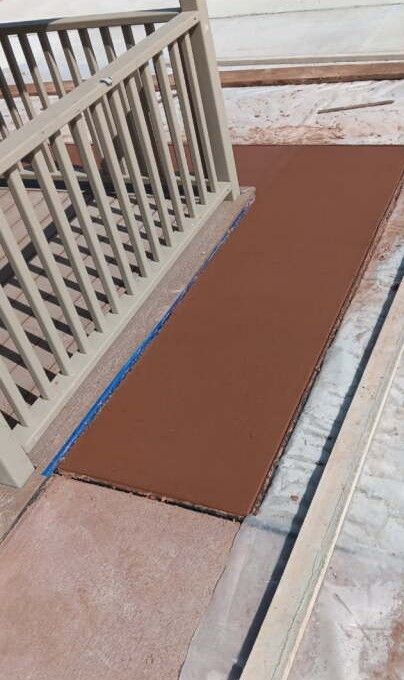 Brown painted concrete walkway next to a beige railing. Blue tape protects the edges.
