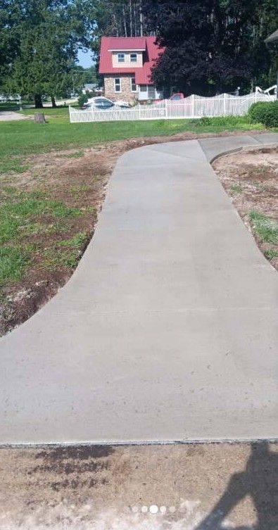 Concrete sidewalk curves through grass toward a house with a red roof.