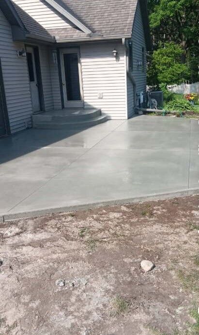 Newly poured concrete patio next to a house with a door, steps, and siding.