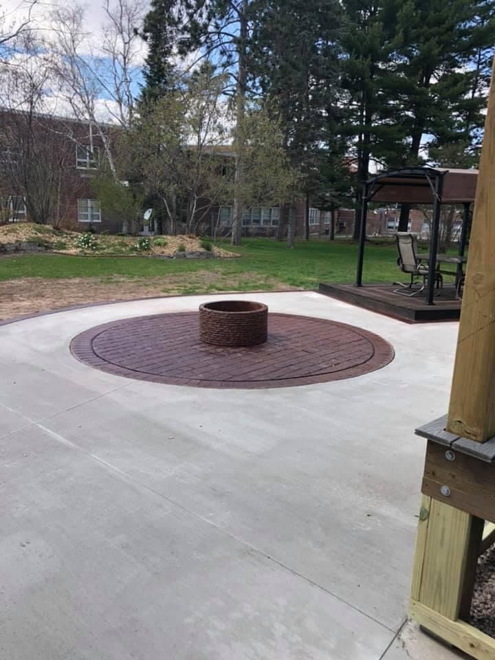 Concrete patio with a circular brick fire pit and a wooden deck under a gazebo.
