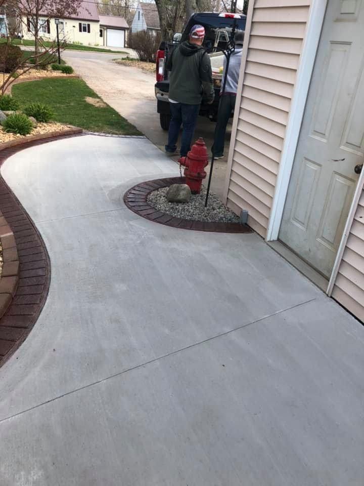 People stand by a black truck near a newly poured concrete driveway and red brick borders.