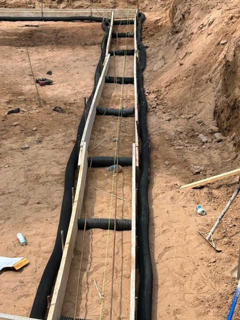 Construction site with wooden forms and reinforcing bars set in a trench for a concrete foundation.