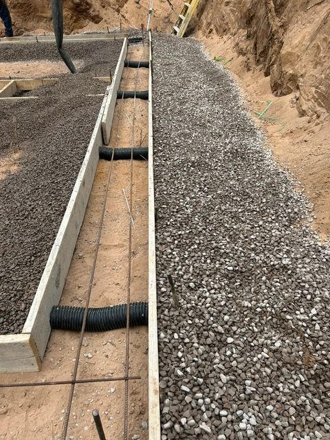 Concrete foundation construction with gravel, forms, rebar, and drain pipes.