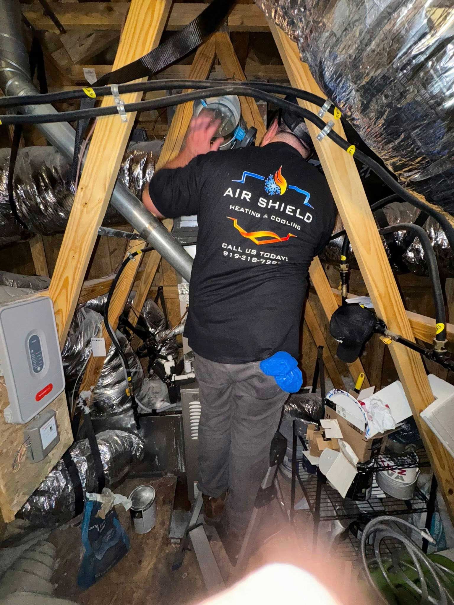 Man in attic, wearing Air Shield shirt, working on HVAC ductwork.