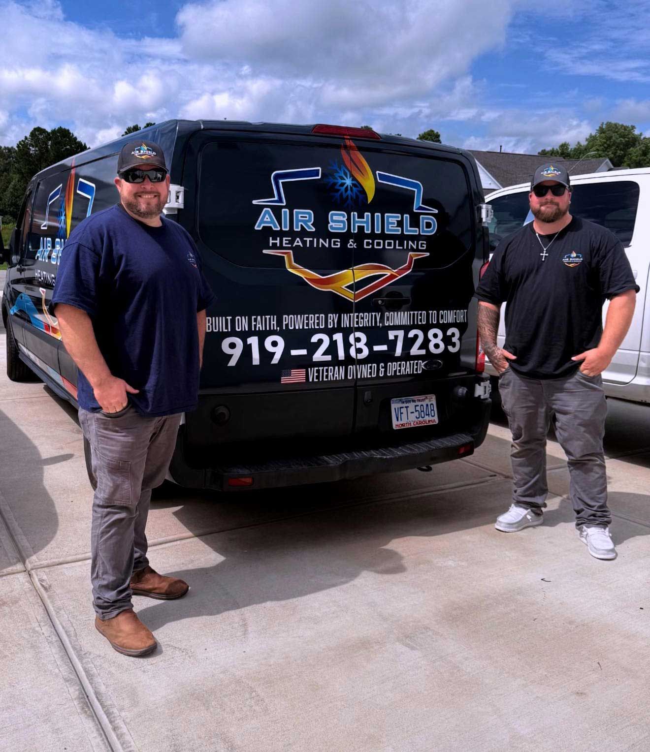 Two men stand in front of a black Air Shield van. The van has a logo and phone number.