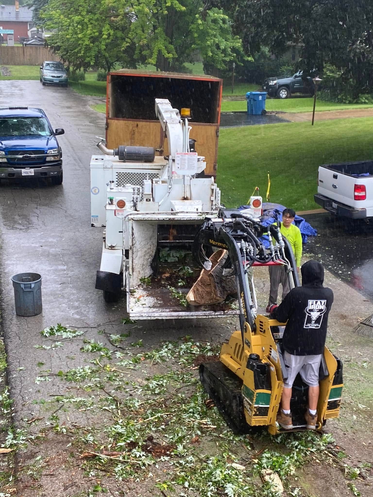 A man is standing next to a tree chipper in a driveway.