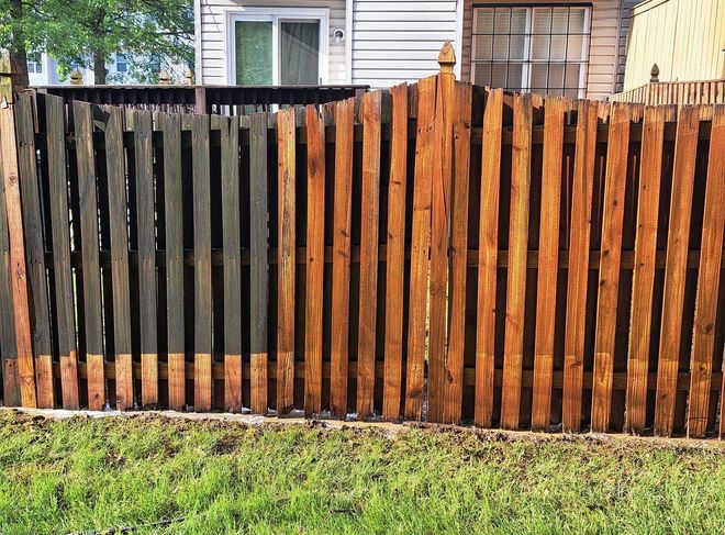 Black-and-brown wooden fence in front of a house and green grass