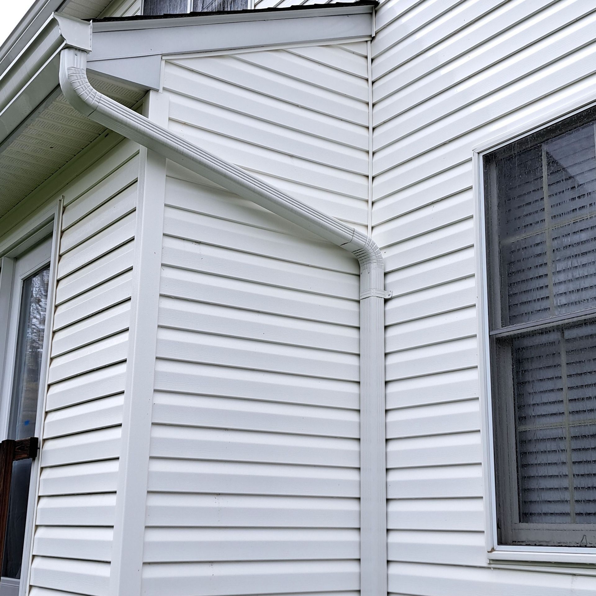 White vinyl-sided house exterior with a window and roof eaves.