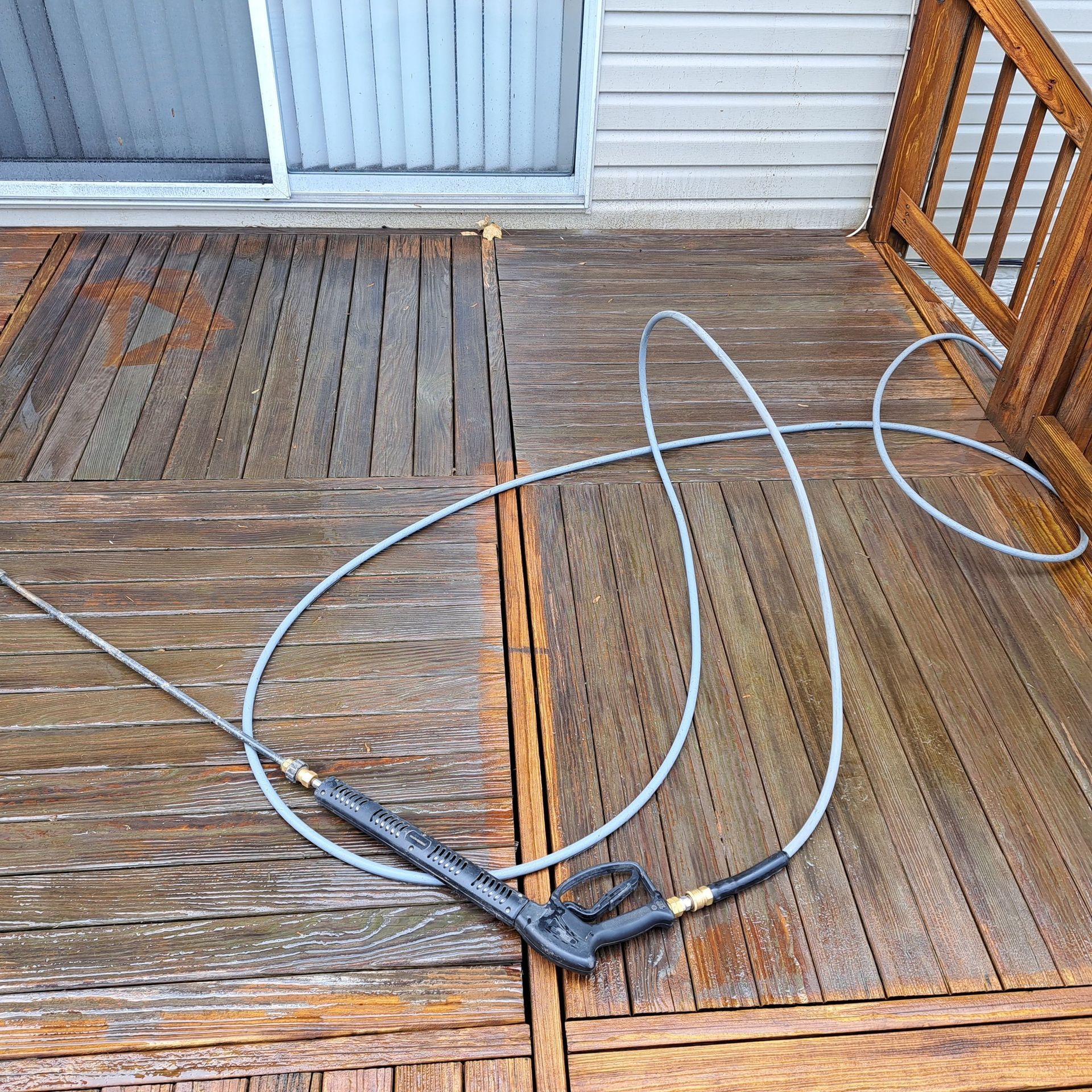 Pressure-washing a wooden deck with a hose and spray wand, water streaks visible.