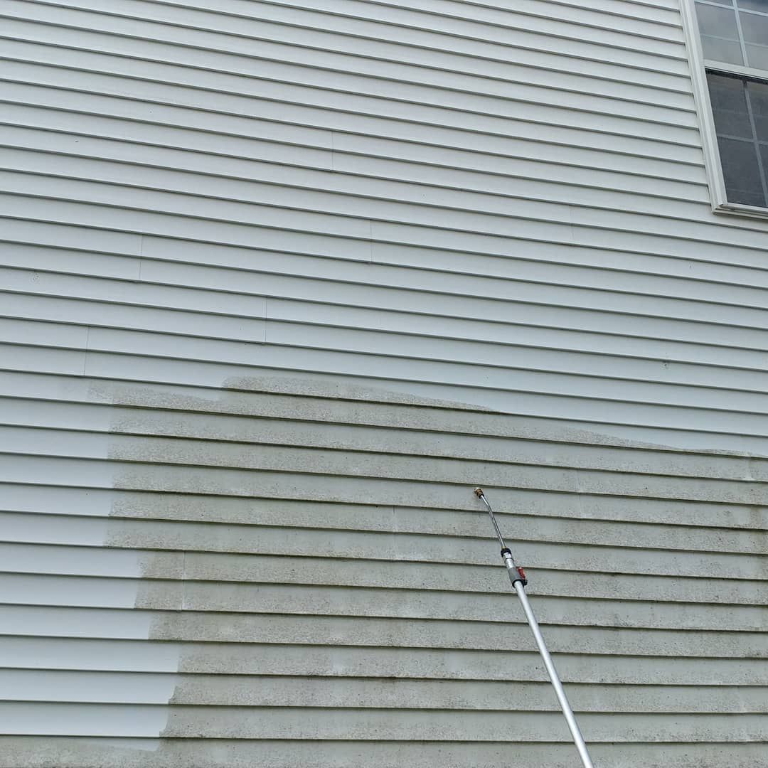 Person pressure-washing stained white house siding with a long wand