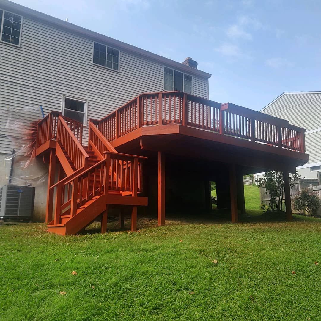 Red wooden backyard deck with stairs attached to a white house over a grassy yard