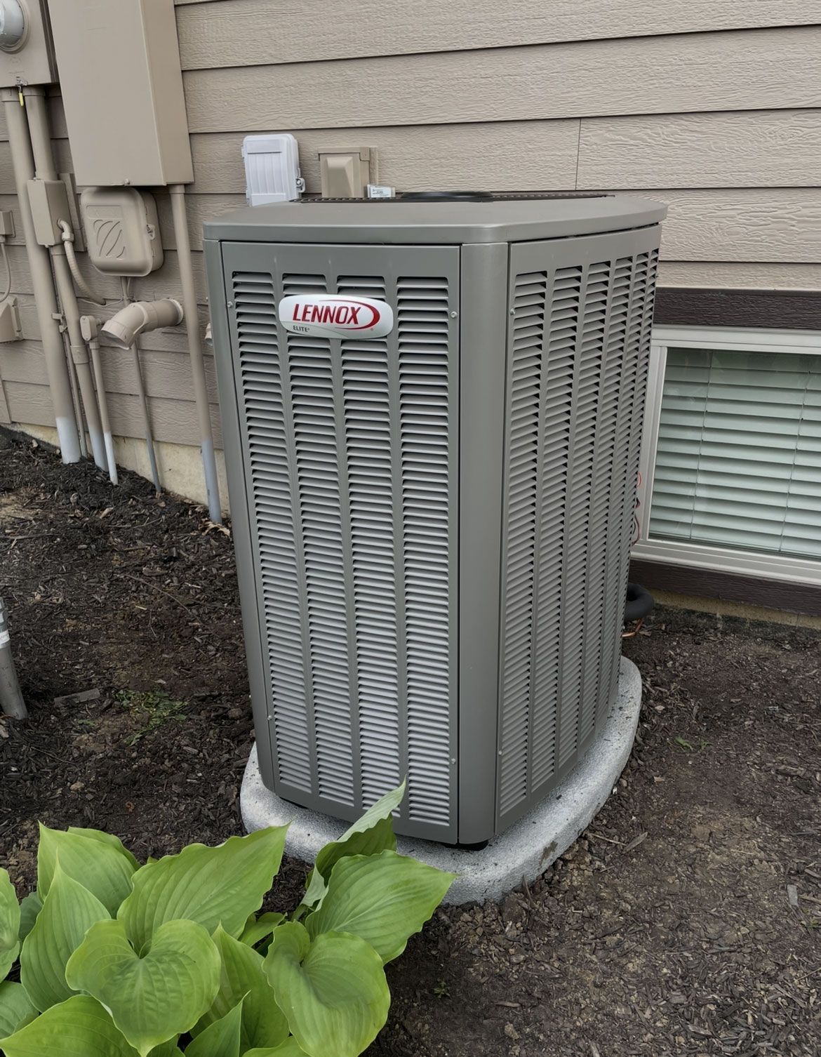 Gray outdoor air conditioner unit beside a house, near siding and basement window.
