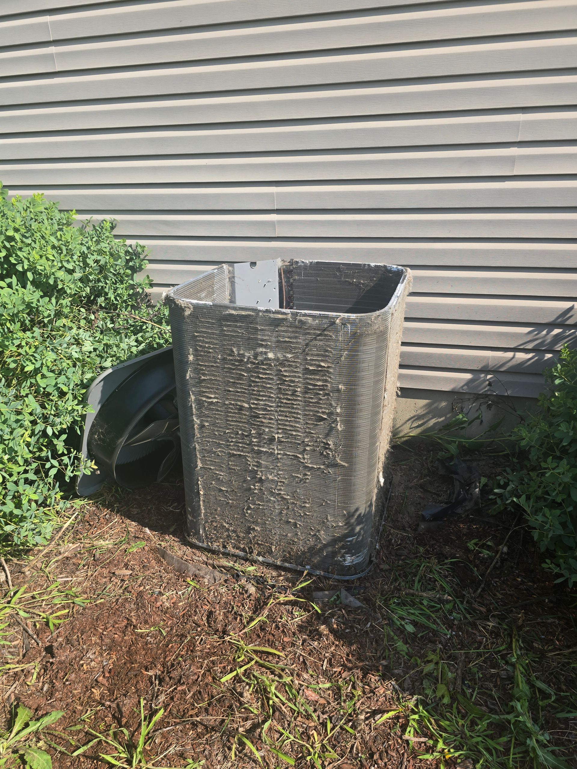 Outdoor air conditioner unit beside a house, partially covered by a textured metal screen.