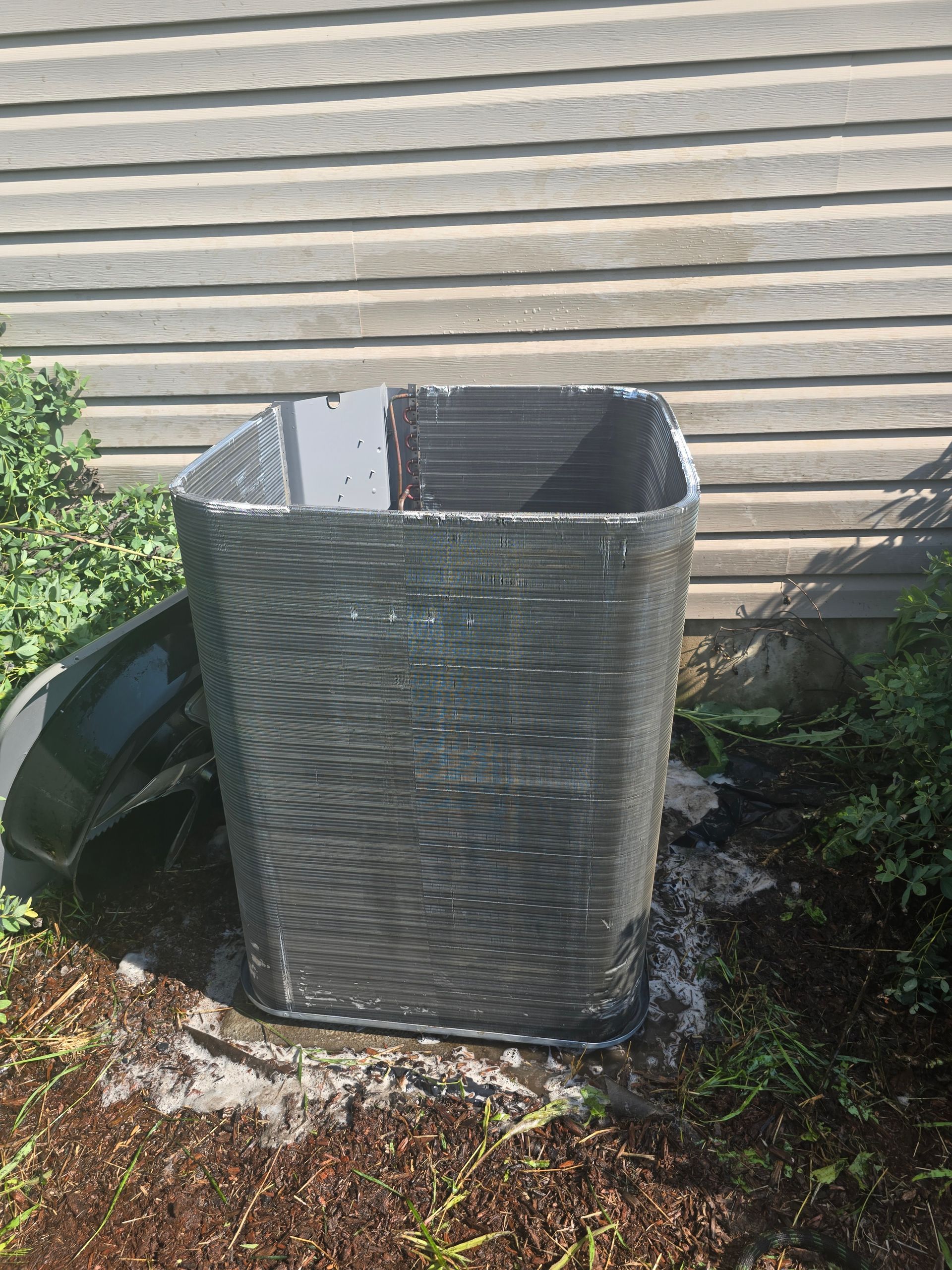 Open-top gray mesh trash bin beside a house wall on a patch of ground