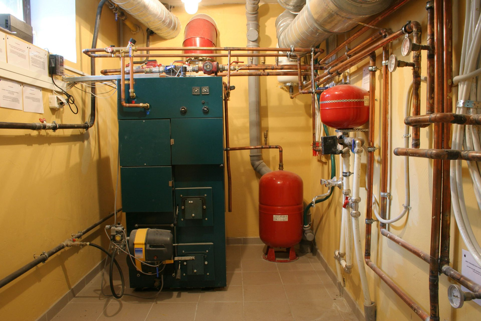 A green heating boiler system with copper pipes and two red expansion tanks in a utility room.