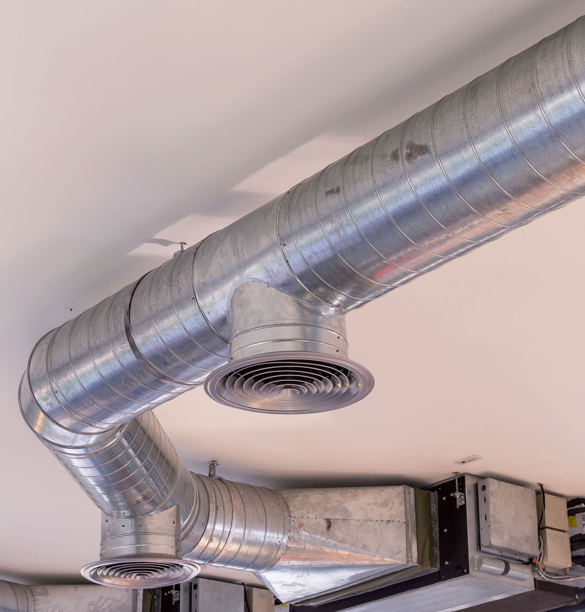 Metallic, cylindrical HVAC ductwork with two circular diffusers installed on a plain white ceiling.