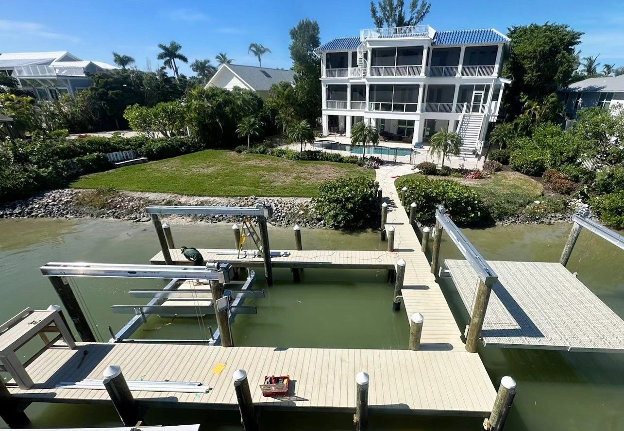Coastal home with dock and boat lift overlooking water. Blue roof and white exterior.