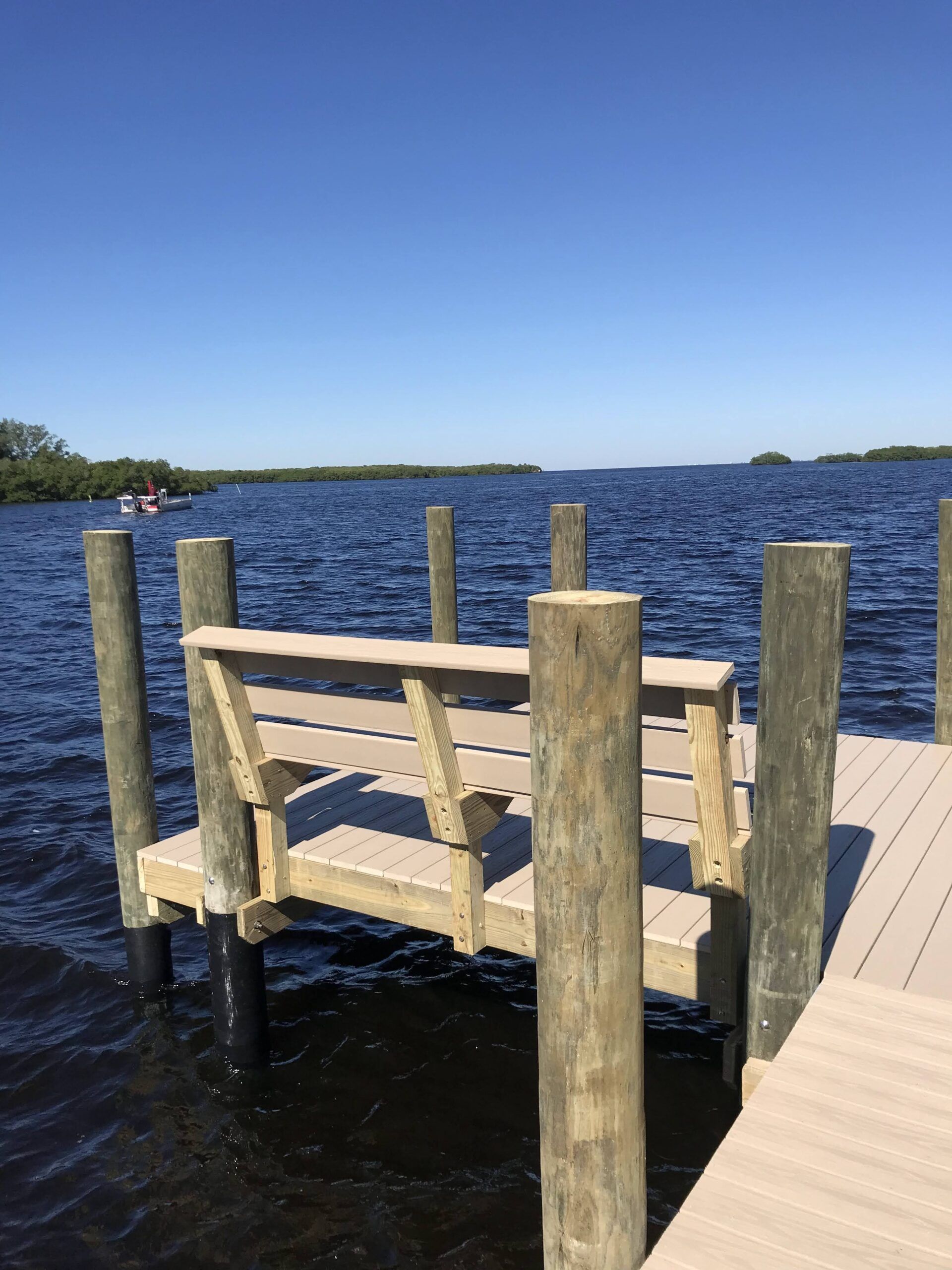 Dock with bench overlooking blue water, trees in the distance under a clear sky.