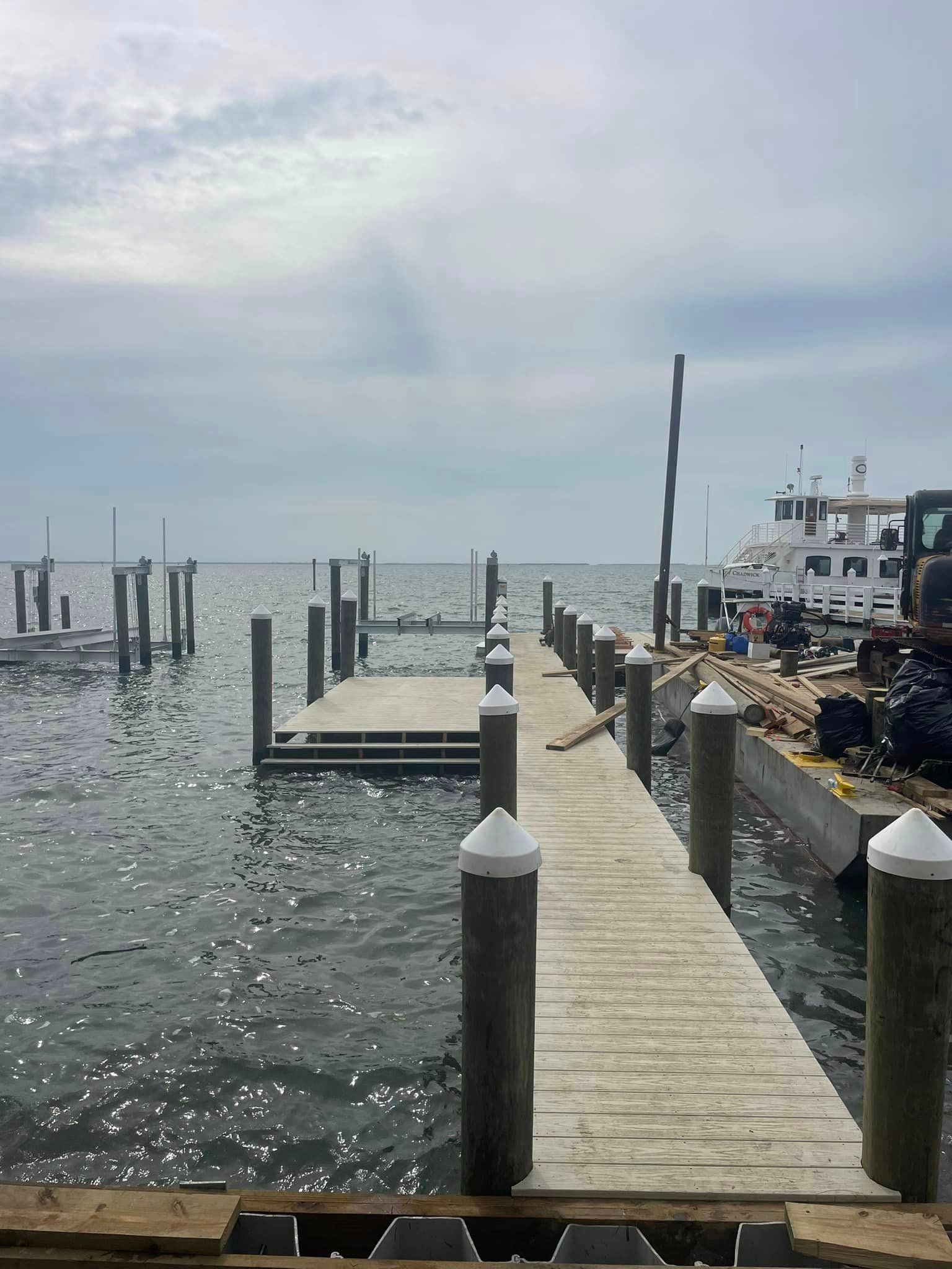 A wooden pier with pilings extends into water under a cloudy sky. A boat is docked nearby.