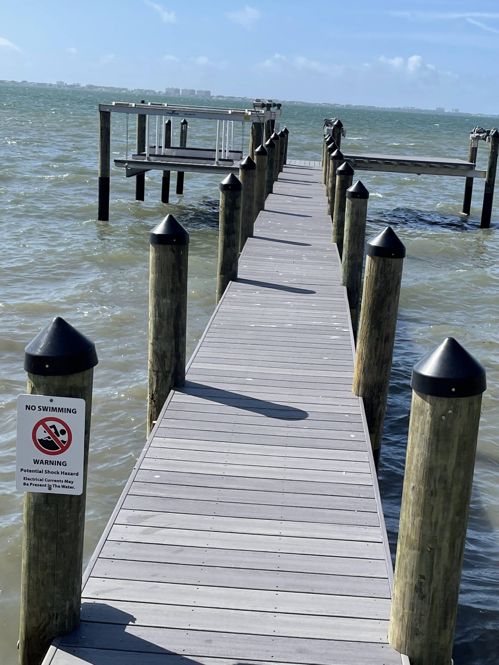 Wooden pier with gray surface extends into choppy water; cloudy sky in background.
