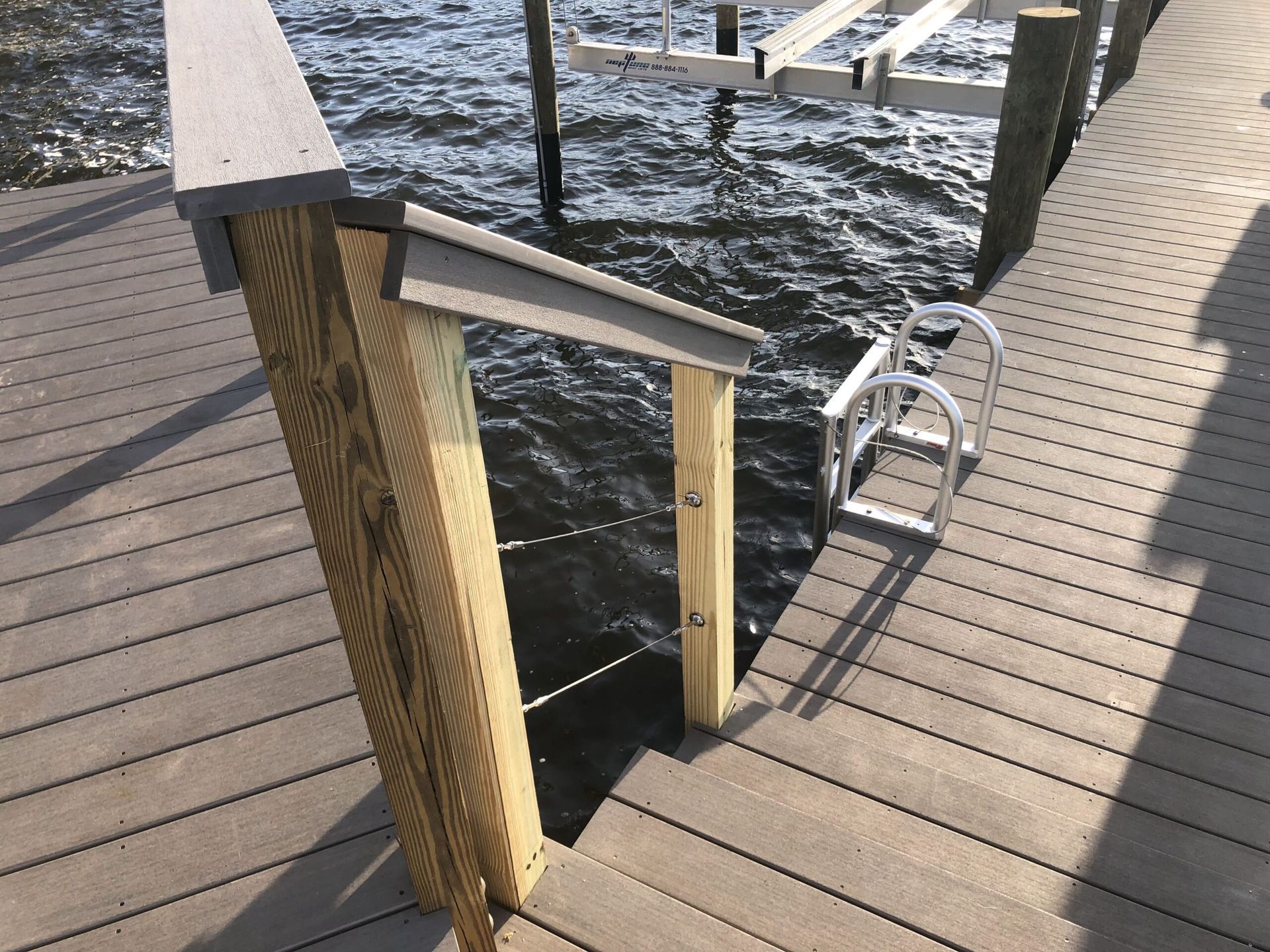 Wooden dock with steps leading to water, handrails, and a ladder.