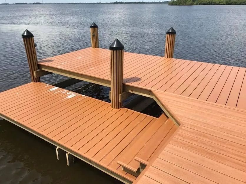 Brown wooden dock extending into calm water, with pilings topped with black caps.
