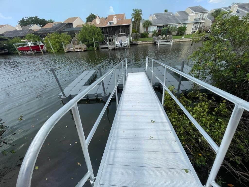 Aluminum ramp leading to floating dock on water, with houses in background.