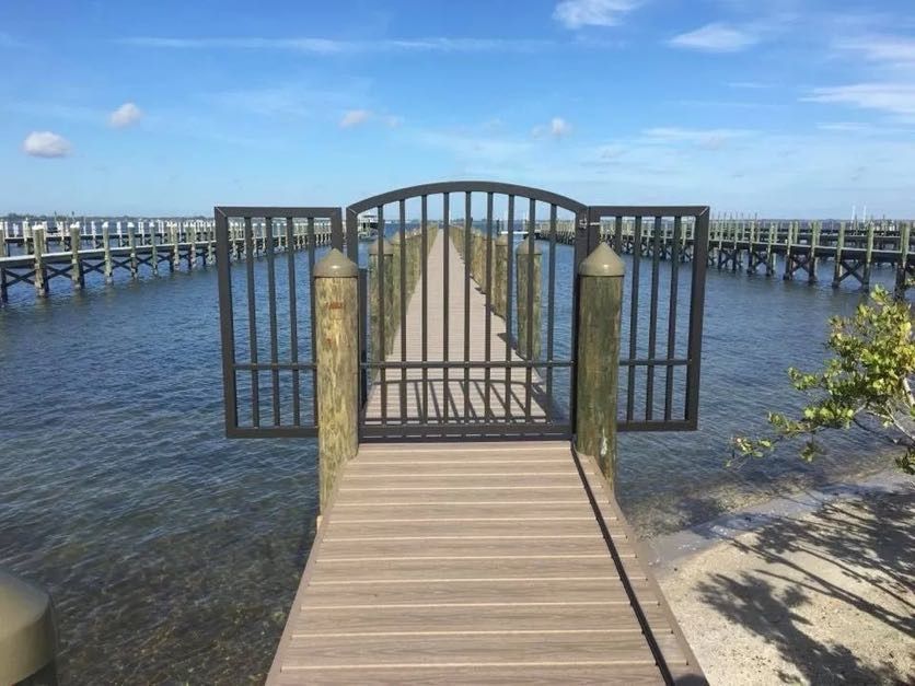 Wooden dock extending into water, with black metal gate and surrounding piers. Blue sky.