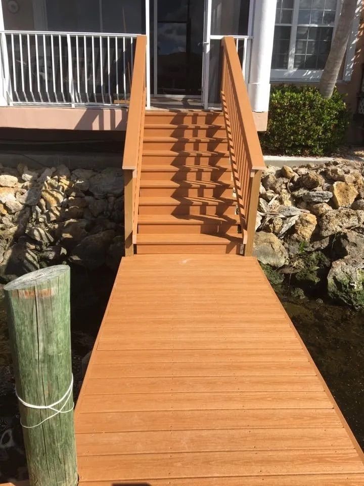 Wooden dock and stairs leading up to a house with white railing.