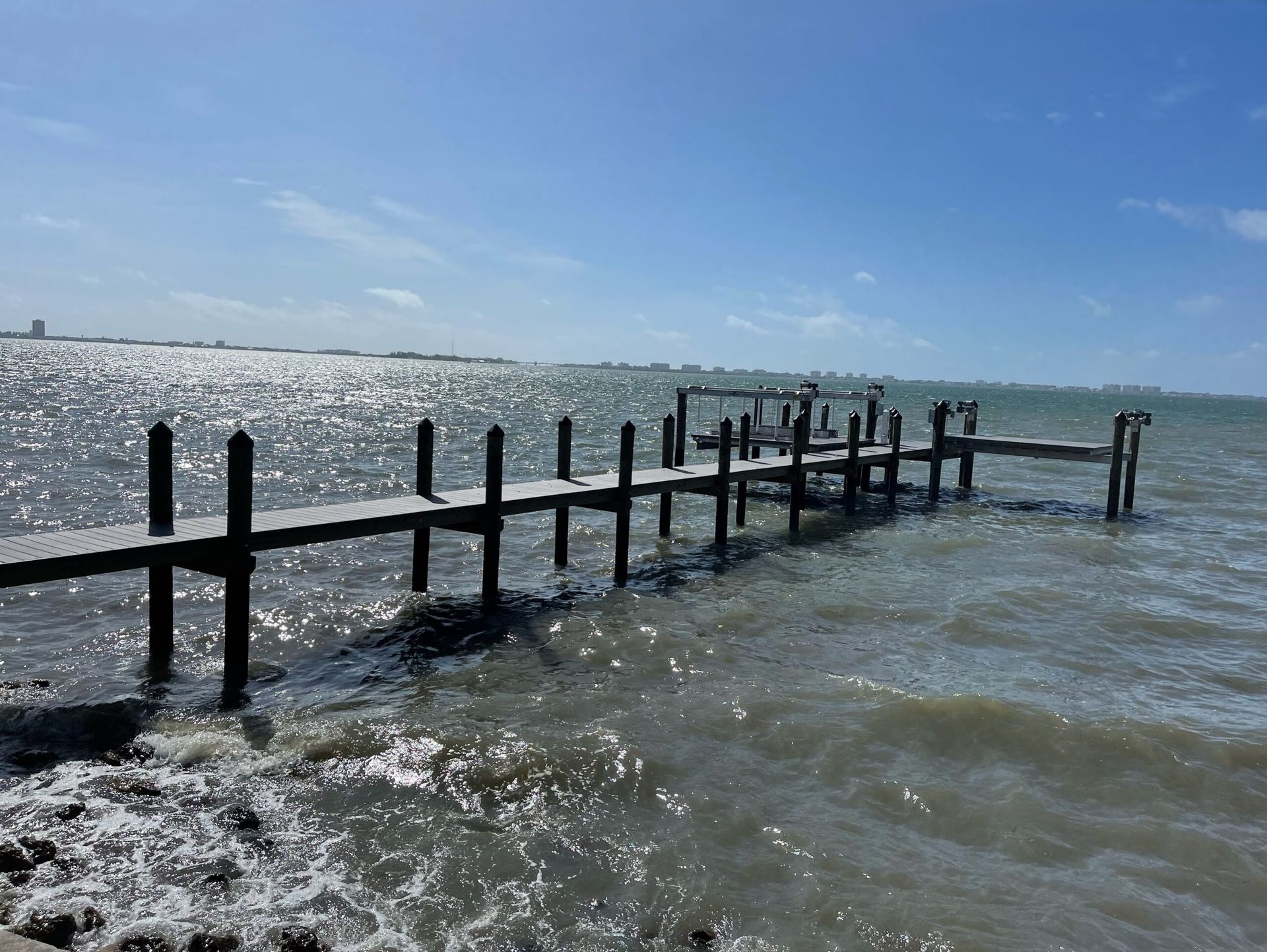 Wooden pier extending into sparkling water under a bright blue sky.