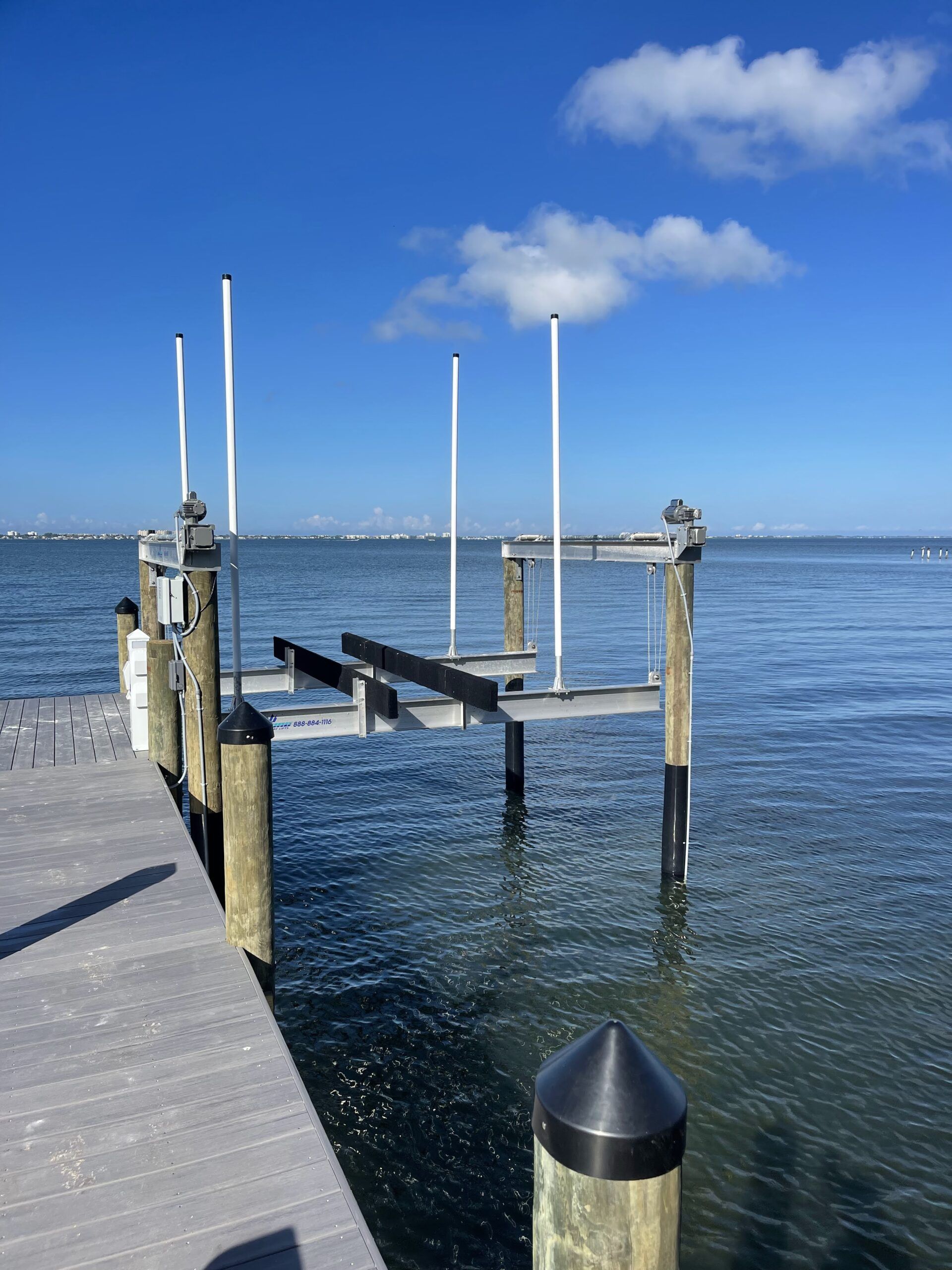 Dock with boat lift over water, sunny day, blue sky, white clouds.