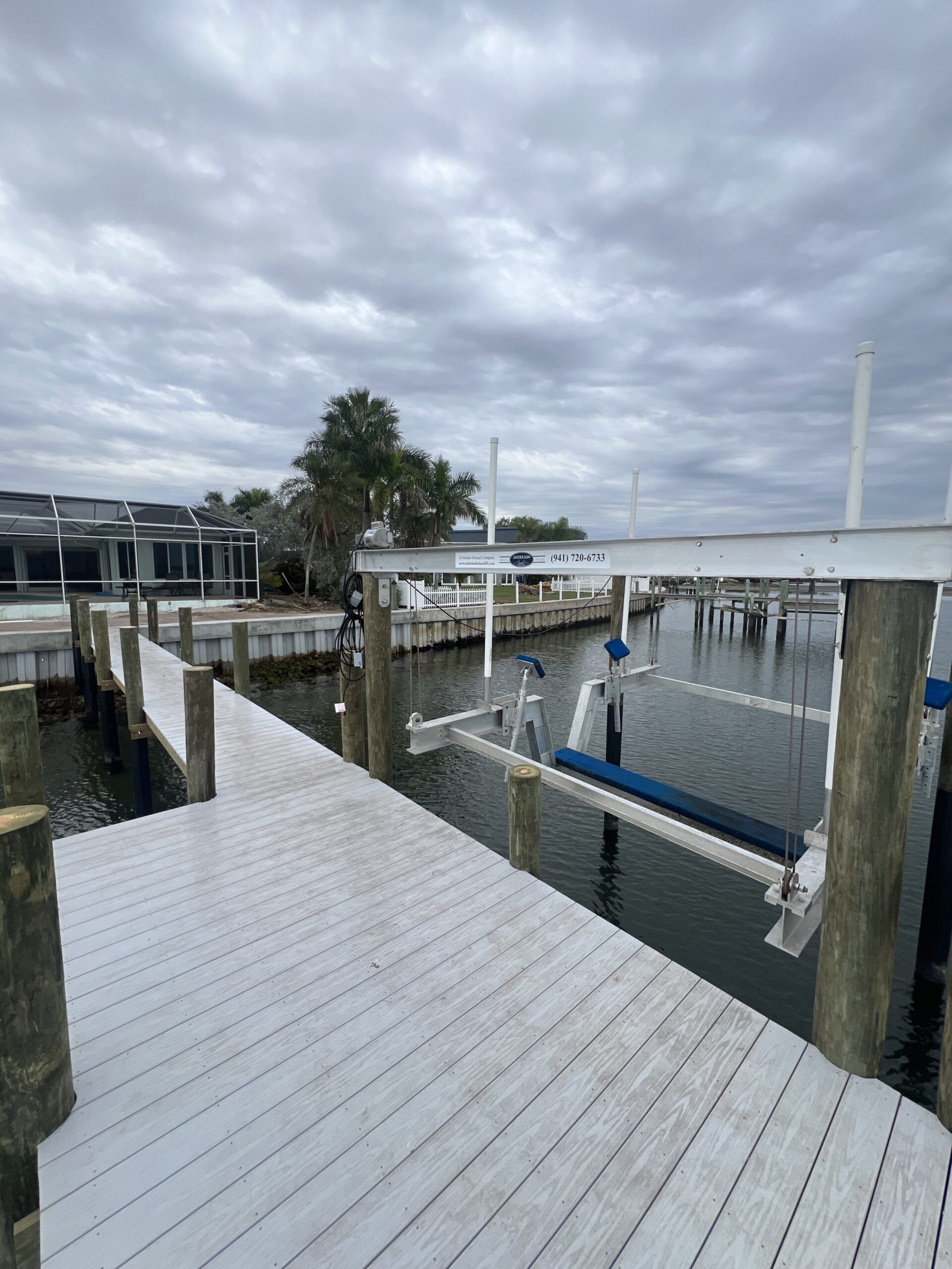 Wooden dock with boat lift over water, cloudy sky overhead.