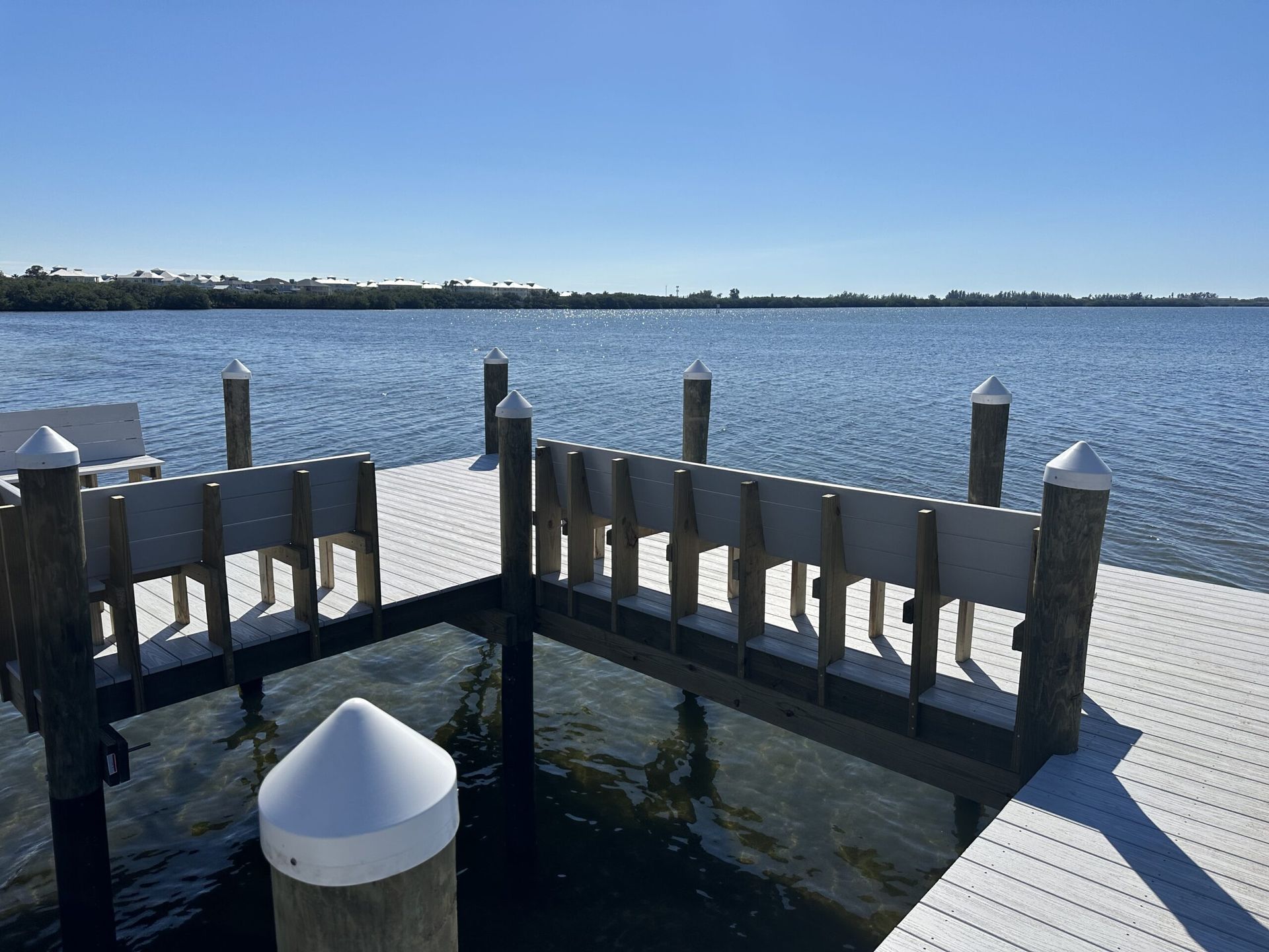 Dock overlooking calm water, clear blue sky. Wooden posts with white tops, grey railings.