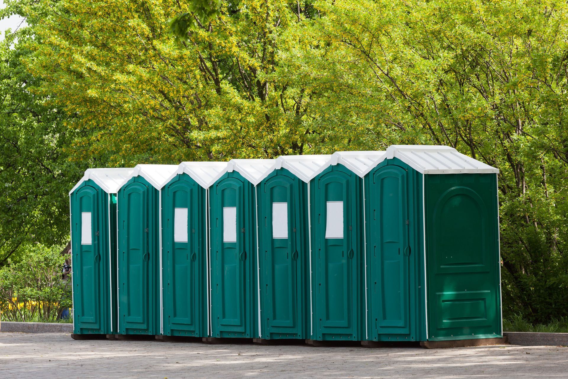 Green portable toilets lined up in front of trees.