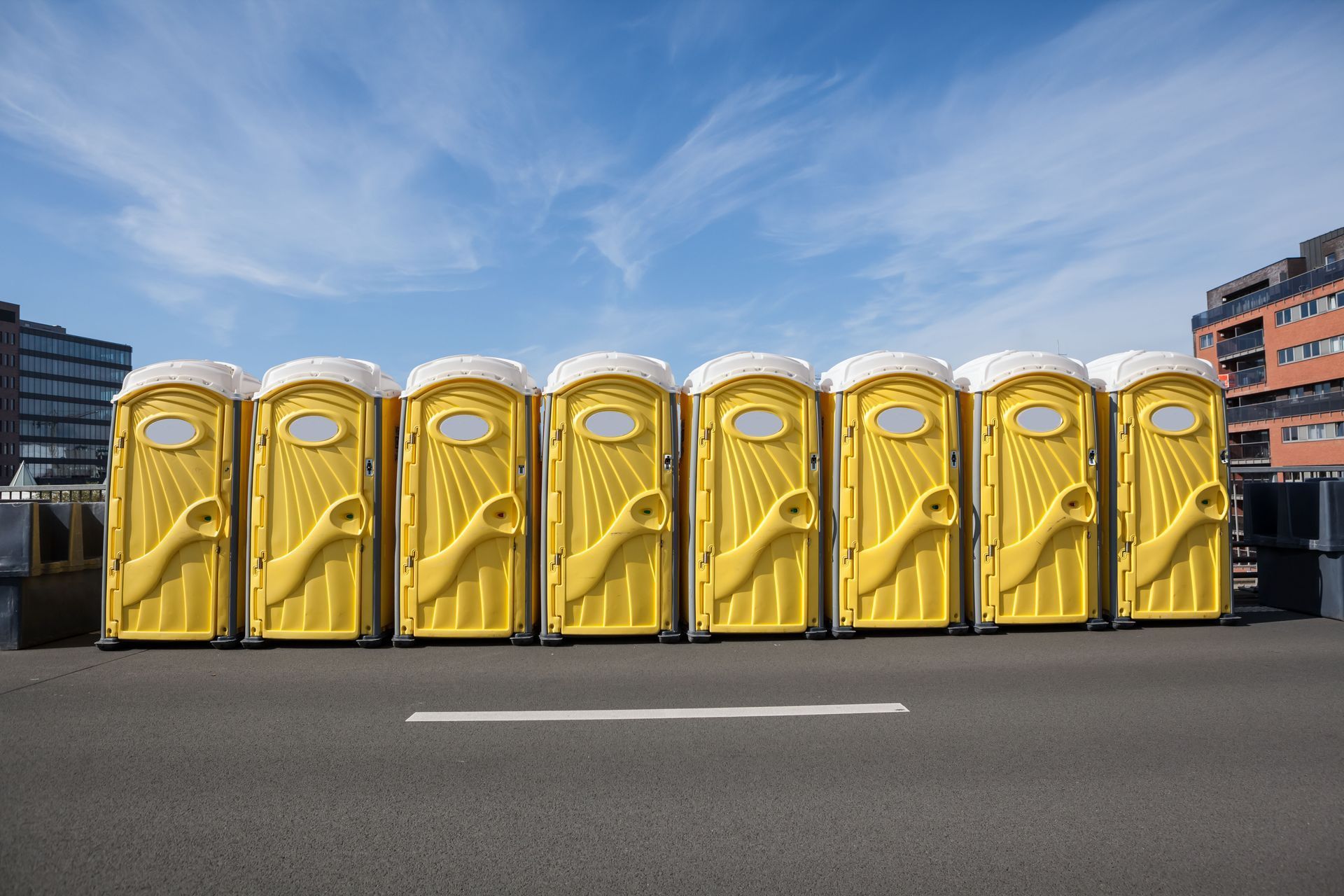 Line of yellow portable toilets on a road, under a blue sky.