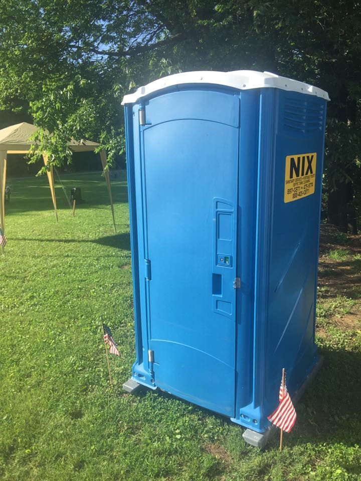 Blue portable toilet on green grass with flags, in a sunny outdoor setting.